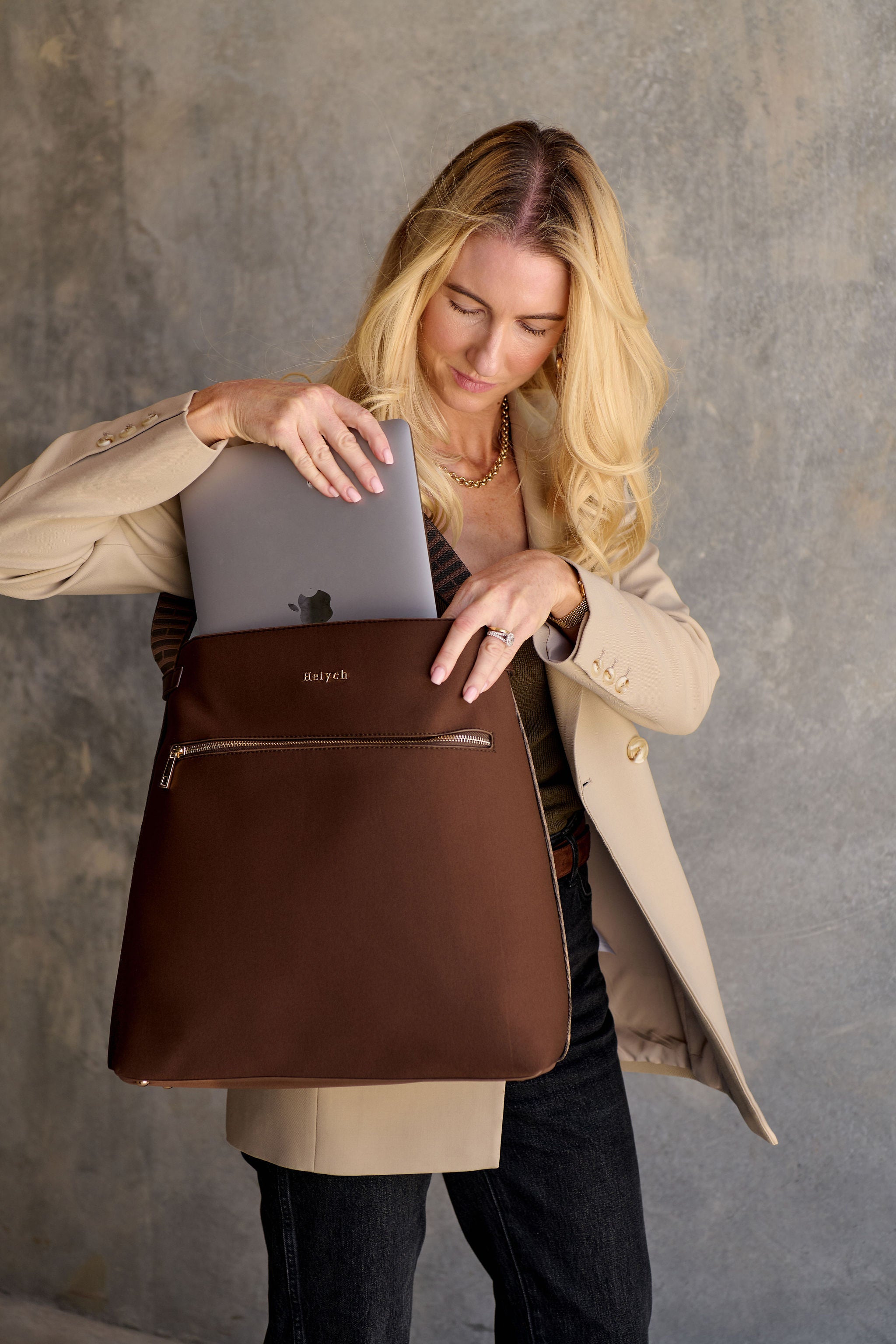 Woman holding a chocolate brown backpack with a gray laptop inside against a gray background