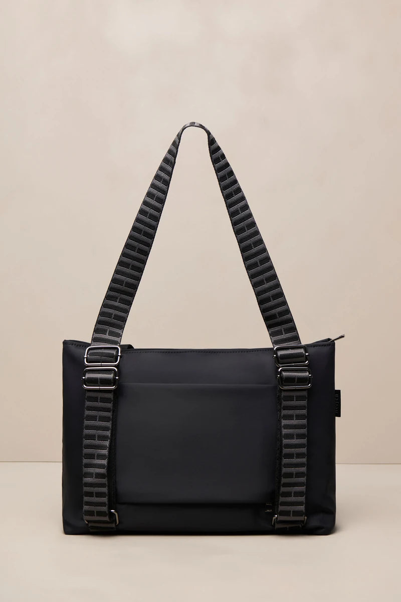 A black nylon shoulder bag with distinctive ribbed black straps and silver-tone hardware, set against a neutral beige background.