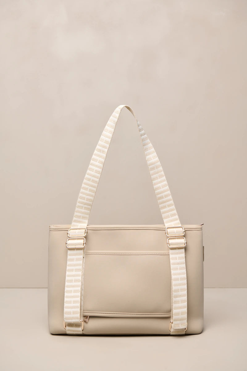 A structured taupe beige tote bag with wide, cream-and-beige striped shoulder straps and gold-tone hardware, set against a neutral beige background.