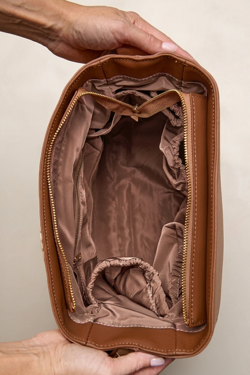Cognac nylon bag held open by a hand on a beige background