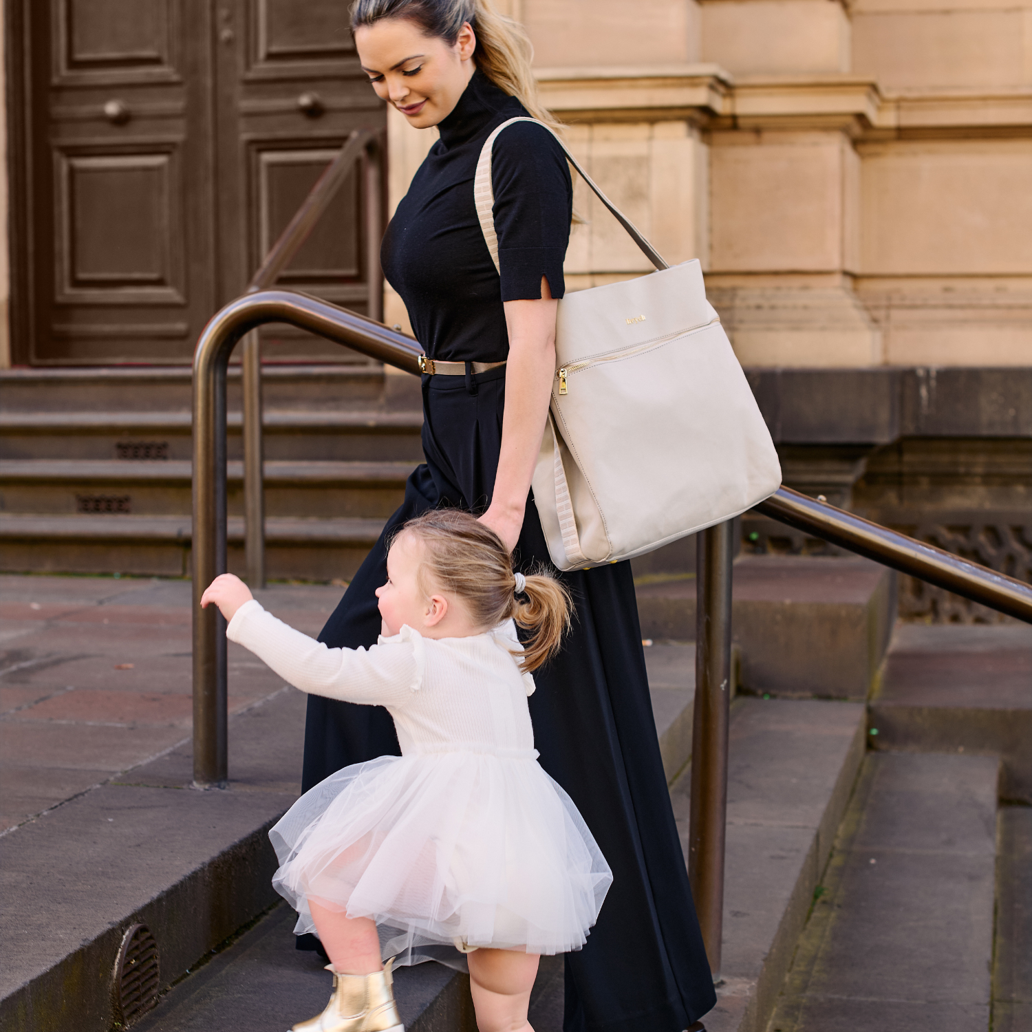 Mum carrying taupe neoprene bag over her shoulder and holding her child's hand