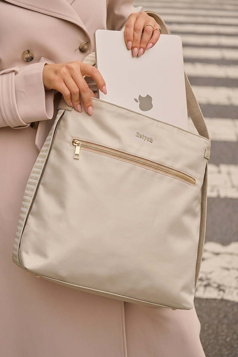 Taupe beige tote backpack held by a women wearing a trench coat, with a blurred background.
