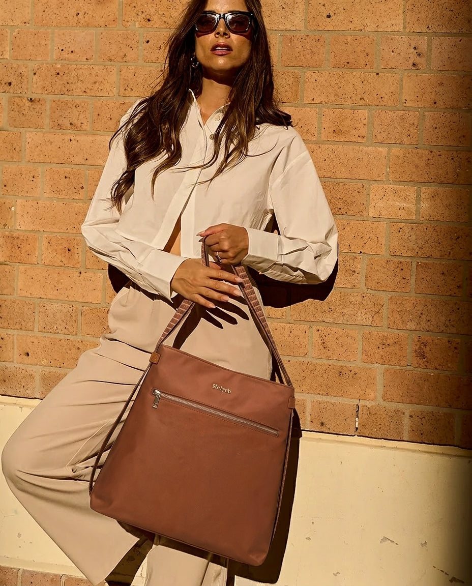 Woman holding a cognac tan bag against a brick wall