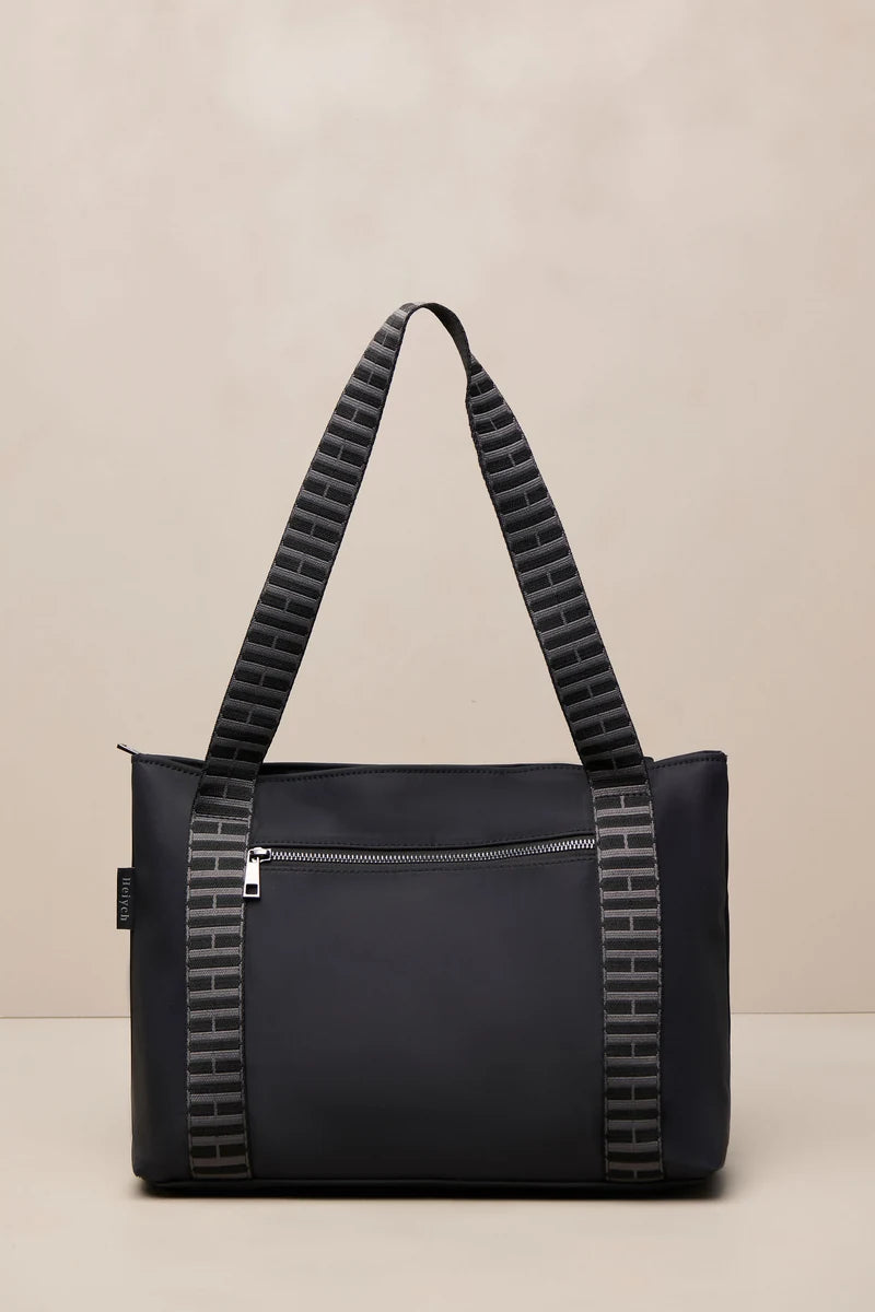 A black tote bag with textured gray and black patterned shoulder straps, shown against a neutral beige background.