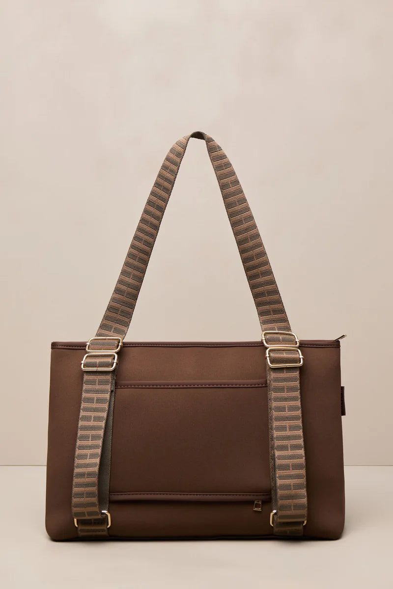 A brown chocolate shoulder bag with wide, patterned brown and beige woven straps and gold-tone hardware, photographed against a neutral beige background.