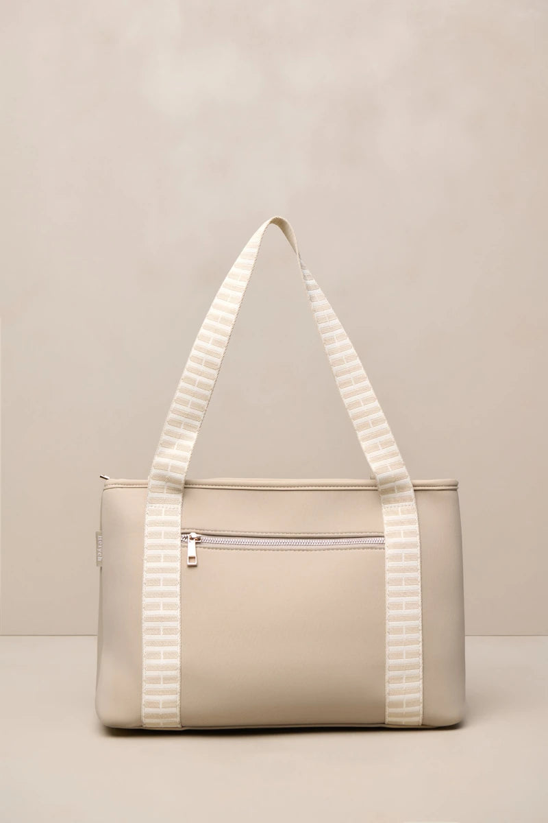 A structured beige taupe tote bag with cream and beige striped shoulder straps, featuring a front zippered pocket and a top zipper closure, set against a neutral beige background.